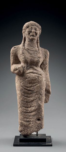 null Statue representing a standing kore, with her parotid locks falling on her shoulders.
Grey...