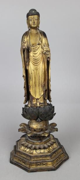 null Bouddha en bois doré debout et vêtu d’un drapé sur des fleurs de lotus. Base...
