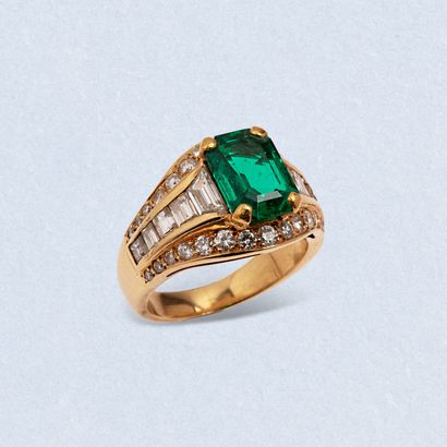  An 18K (750) yellow gold ring centered on a claw-set step-cut emerald set with trapeze...