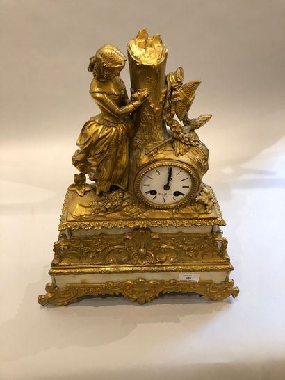 null A gilt bronze clock resting on a white marble base depicting a young woman engraving...