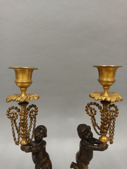 null A pair of candlesticks decorated with cherubs in black patina bronze with a...