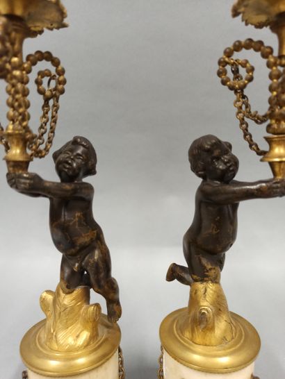 null A pair of candlesticks decorated with cherubs in black patina bronze with a...