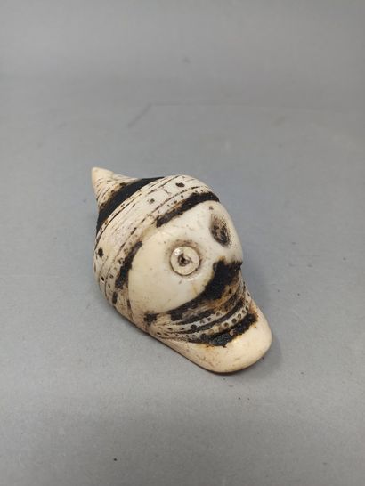 null Shell pendant carved in the shape of a skull and partially covered with tar....