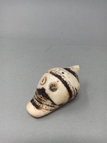 null Shell pendant carved in the shape of a skull and partially covered with tar....