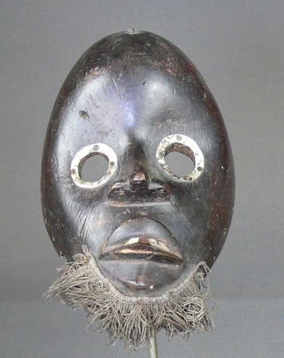 null Wooden racing mask with a dark patina showing an oval face with metal rimmed...