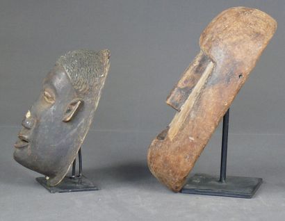 null Deux masques en bois léger, l'un à patine sombre figurant un visage naturaliste...