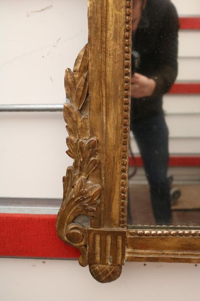 null A mirror, the frame in wood and gilded stucco, the pediment decorated with a...