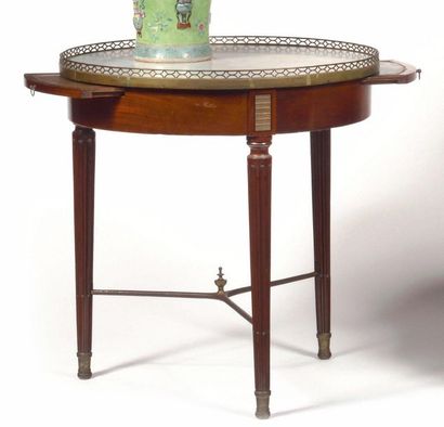 null A mahogany circular table opening to one drawer and two sliding shelves, the...