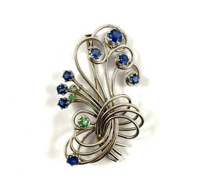 null A brooch decorated with a design of scrolls holding emeralds and sapphires....