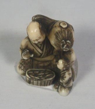 JAPON Netsuke en ivoire sculpté et patiné représentant un tabletier et un enfant....