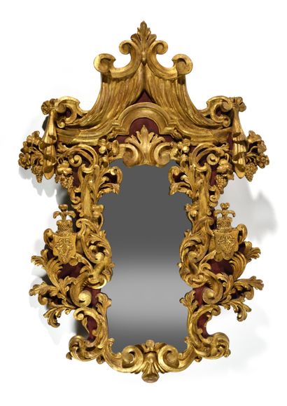 null A carved and gilded painted wood contoured mirror, richly decorated with foliage,...