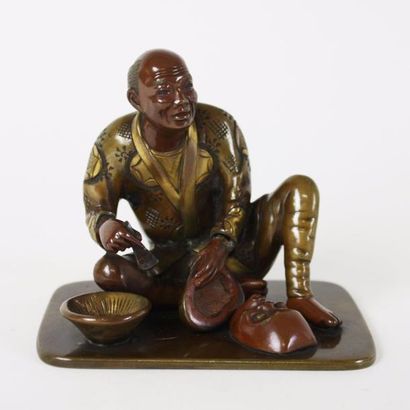  JAPON Figurine en bronze à deux patines représentant un homme assis au sol sculptant...