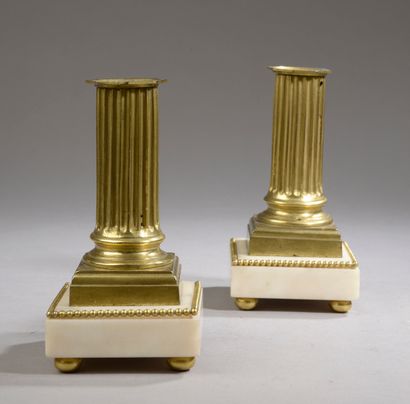 null A pair of small ormolu and white marble candlesticks, the shaft in fluted half-column,...