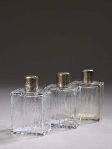 Suite of three grooved glass bottles, the...