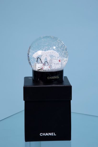 null CHANEL. 
Glass snow globe on black lacquered plastic base featuring the double...