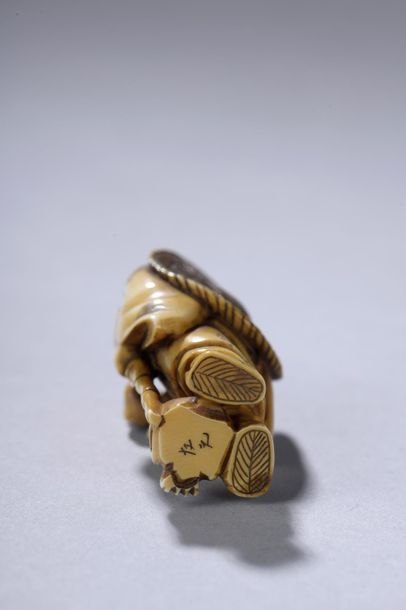 null JAPON, début du XXe siècle. 
Netsuke signé figurant un homme debout tenant dans...