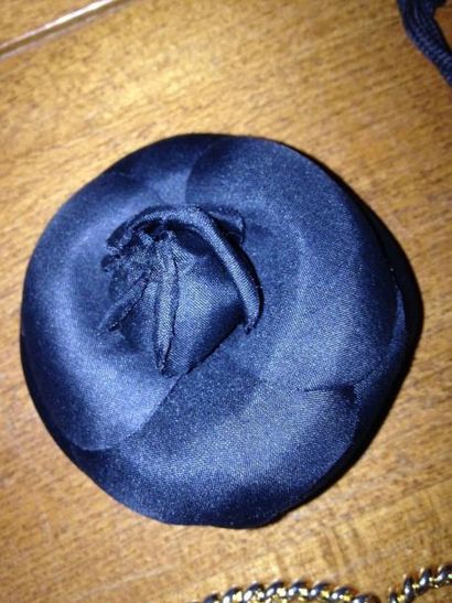 CHANEL 
BROCHE camélia en soie noire, signée.
Diam.: 7 cm
Dans sa boîte