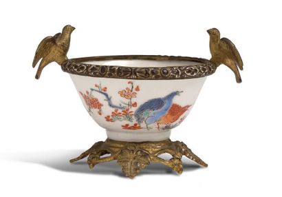 JAPON FIN DE LA PÉRIODE EDO (1603-1868), XIXe SIÈCLE 小垣门瓷碗，装在有凹槽的青铜座上，边上有一个青铜圆圈，上面有两只伸开翅膀的鸟。
碗边饰有蓝色和红色的鹌鹑，碗内有一棵蓝色山水背景的树。
高共：7,4厘米-深7,6厘米
...