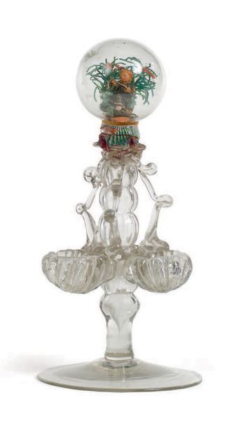 null 来自奥尔良的两件玻璃制品
- 一个无色的玻璃调味品架，有一个空心轴，三个贝壳从里面冒出来。它的顶部是一个空心球，里面有一个彩色蜡制的小耶稣，手持十字架，在珍珠的植物圈里。奥尔良，18世纪初。
高度：25厘米...