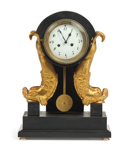 一个黑漆木制的多芬钟，两边是两个圆雕的鎏金木海豚。白色珐琅的表盘镶嵌在一个圆形的鎏金铜框中，用阿拉伯数字显示小时。它安放在四个扁平的圆圈脚上。修复时期。
高：38.5厘米...