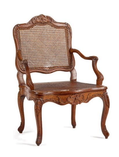 一把木雕藤条扶手椅，上面装饰着锯齿状的贝壳和刺桐叶，椅腿呈拱形。路易十五时期。后来的藤条。
高度：95.5厘米...