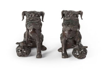 CHINE Paire de chiens de Fô en bronze à patine brune tenant chacun une boule ajourée...