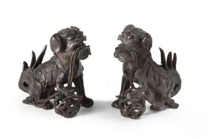 CHINE Paire de chiens de Fô en bronze à patine brune tenant chacun une boule ajourée...