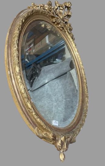 null Oval wood and gilded stucco mirror with laurel leaf motif and ribbon bow pediment....