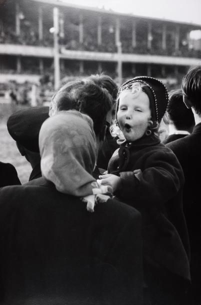 DAVID DOUGLAS DUNCAN (1916) Petite fille dans les bras de sa mère, dans les tribunes...