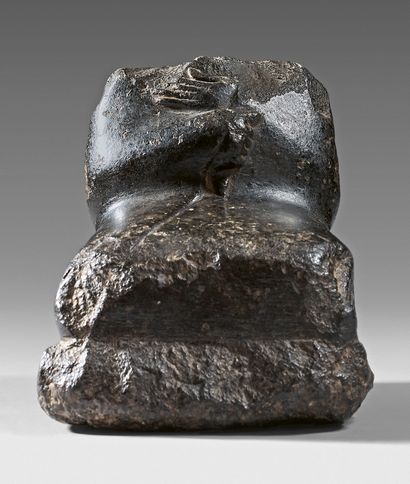  Statuette acéphale assise en tailleur et emmitouflée dans un manteau. Diorite. Égypte,...