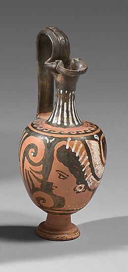  A red-figured oenochoe on a pedestal with a woman's head in left profile. Under...