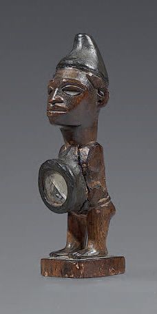 Fétiche Kongo (Congo) The figure with glass encrusted eyes and wearing a cap is shown...