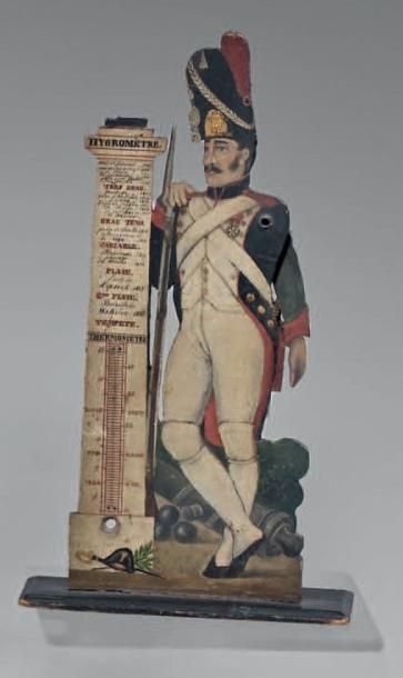 null Thermomètre en bois peint représentant un canon debout contre lequel un grenadier...