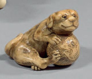 JAPON Netsuke en ivoire, un chien assis jouant au ballon de ke­mari. Les yeux sont...