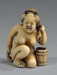 JAPON Netsuke en ivoire, représentant une femme nue accrou­pie, essuyant le dos avec...