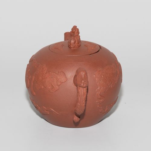 Teekanne 茶壶

中国。宜兴陶器。棕红色的身体上有护卫狮子的浮雕，玩弄着彩带。盖子上有雕刻的护卫狮子作为把手。高10厘米。- 略有磨损。