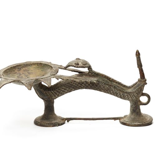 A FINE BASTAR BRONZE OIL LAMP 一个精美的巴斯塔青铜油灯
印度，19-20世纪。一盏精美的油灯，下半部分是一个两脚动物的变形，它的头&hellip;