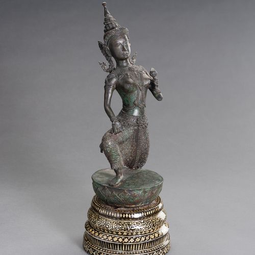 A BRONZE FIGURE OF A DANCING APSARA 一尊跳舞的阿帕拉铜像
柬埔寨，1920年。这尊铜像以生动的姿态跪在莲花苞上，身穿桑普，戴&hellip;