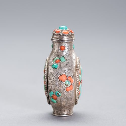 AN EMBELLISHED SILVER SNUFF BOTTLE 一个有纹饰的银质鼻烟壶
中国，19世纪。壶身刻有细微的花叶装饰，上面整齐地镶嵌着珊瑚和绿松&hellip;