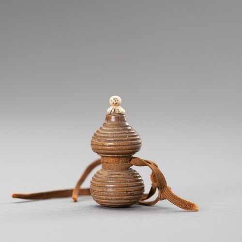 A HYOTAN SHAPE WOOD NETSUKE 一个HYOTAN形状的木制网罩
日本，19世纪

这个网罩是由木头雕刻而成的，用编织绳包裹，上面有一个骨&hellip;