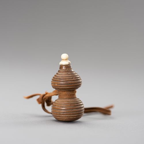 A HYOTAN SHAPE WOOD NETSUKE 一个HYOTAN形状的木制网罩
日本，19世纪

这个网罩是由木头雕刻而成的，用编织绳包裹，上面有一个骨&hellip;