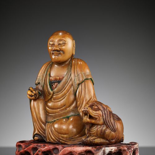A SOAPSTONE FIGURE OF A LUOHAN WITH A BUDDHIST LION, 18TH CENTURY A SOAPSTONE FI&hellip;