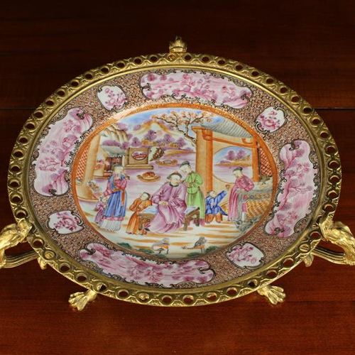 Null 一个清代中国出口的文华老爷车，带有鎏金铜套。盘子用彩色珐琅彩精巧地绘制了一个复杂的人物场景，在尿布的边框中穿插着用粉色描绘的风景图，并与花卉图案交替。&hellip;
