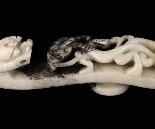 Null 一件18/19世纪的钙化玉Belk钩，带有原始的黑色污渍，雕刻着一条蠕动的蝾螈，有一个龙头的钩端，长3½'' (9厘米)。