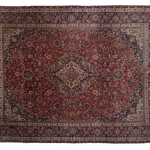 A Kashan rug 一块卡尚地毯，20世纪，红色领域的中心是一个菱形的奖章，装饰着花朵，在一个蓝色的边框内。371x274厘米。