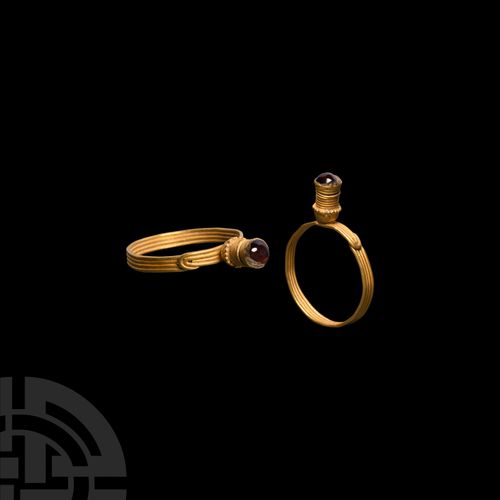 Null 希腊石榴石金戒指，约公元前5-3世纪 一枚金戒指，扁平的戒身由四排金丝组成，圆形的终端在一个肩部重叠，塔形的戒面有盘绕的金属丝体和颗粒状的项圈，镶嵌着&hellip;