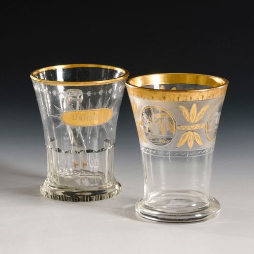2 Andenkenbecher 

2个纪念杯。 
19世纪上半叶。
无色玻璃，金色装饰。高9,5和10厘米。
1个刻面火山口杯，有手柄，刻有花边，正面有金质&hellip;