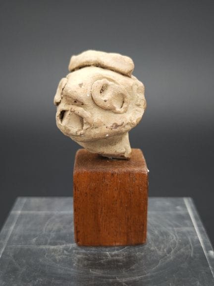 风格化的赤陶人头像，
现代作品，风格仿照前哥伦布时期艺术，
饰有圆点和卷纹的浮雕图案。
底座为后加。