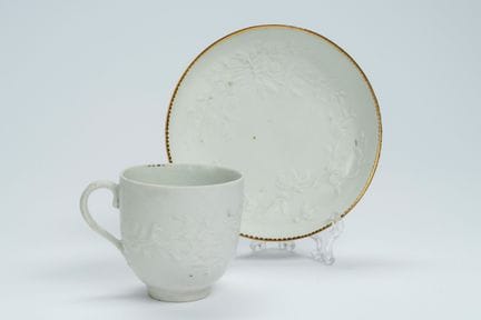 A white porcelain cup and saucer with a relief pat