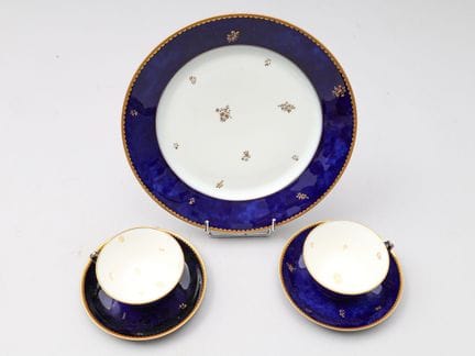 塞夫勒国家瓷器厂 两只瓷杯、两个杯托和一个瓷盘，采用云纹钴蓝釉，饰以狼牙纹和花卉金彩图案。底部印章：
